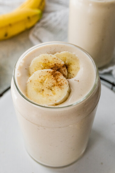 A banana smoothie in a glass, topped with fresh banana slices and a sprinkle of cinnamon.