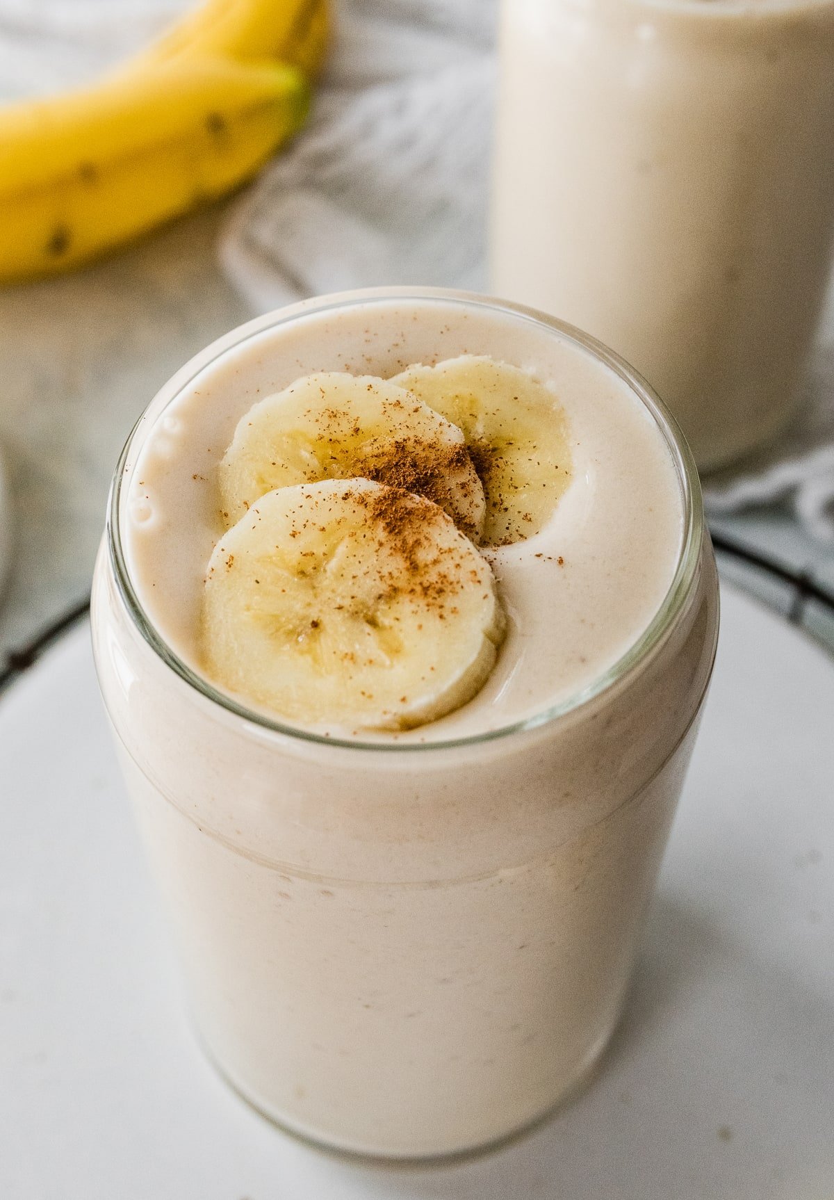 A banana smoothie in a glass, topped with fresh banana slices and a sprinkle of cinnamon.