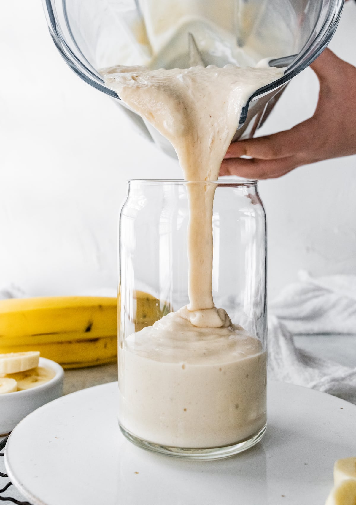 Woman's hand pouring a banana smoothie into a glass.