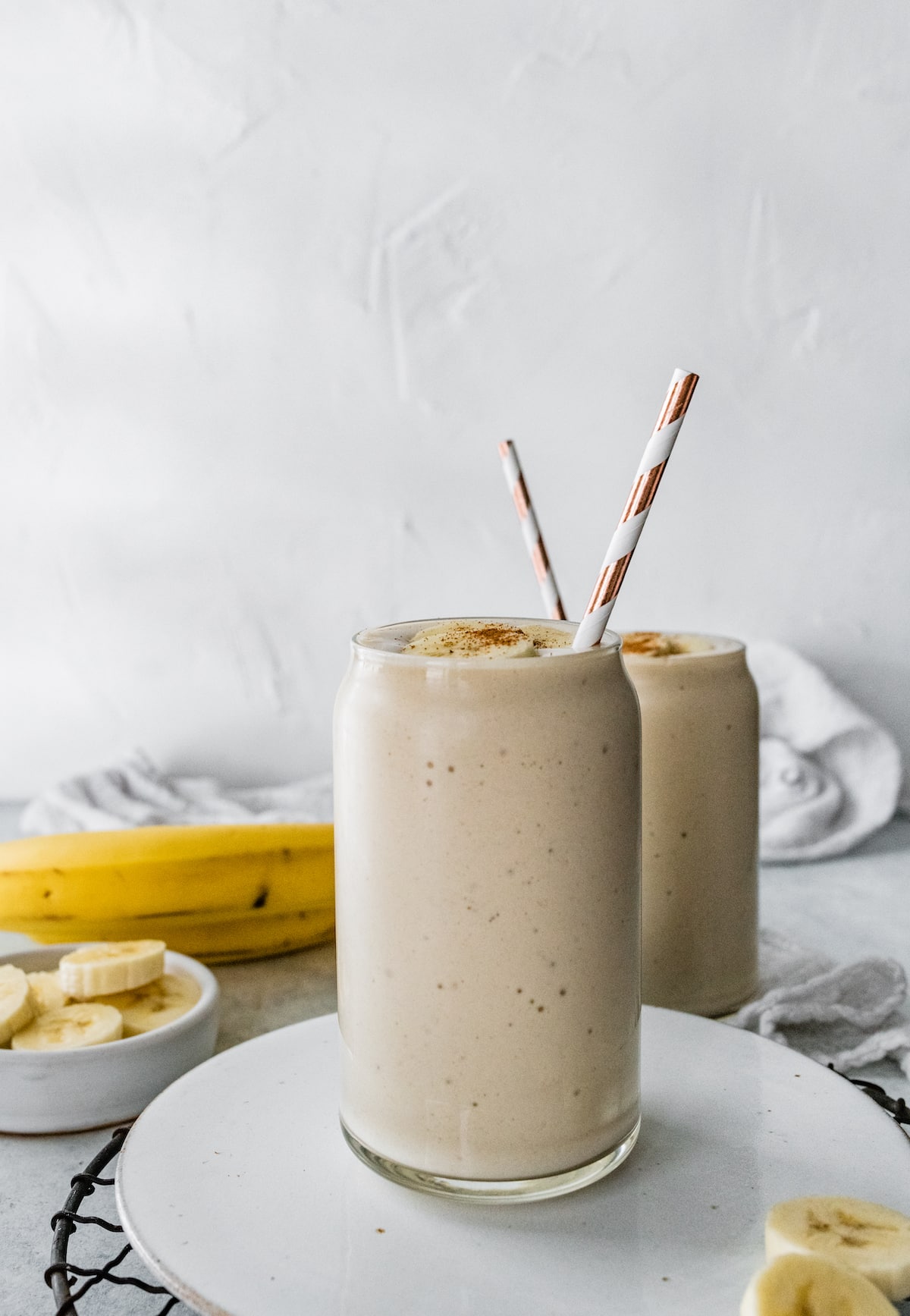 Two banana smoothies in glasses with straws.