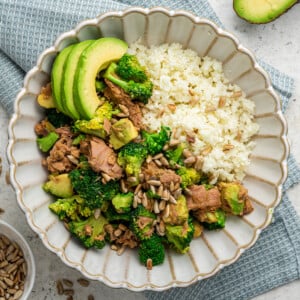 One broccoli avocado tuna bowl topped with sunflower seeds and fresh avocado slices served over rice.