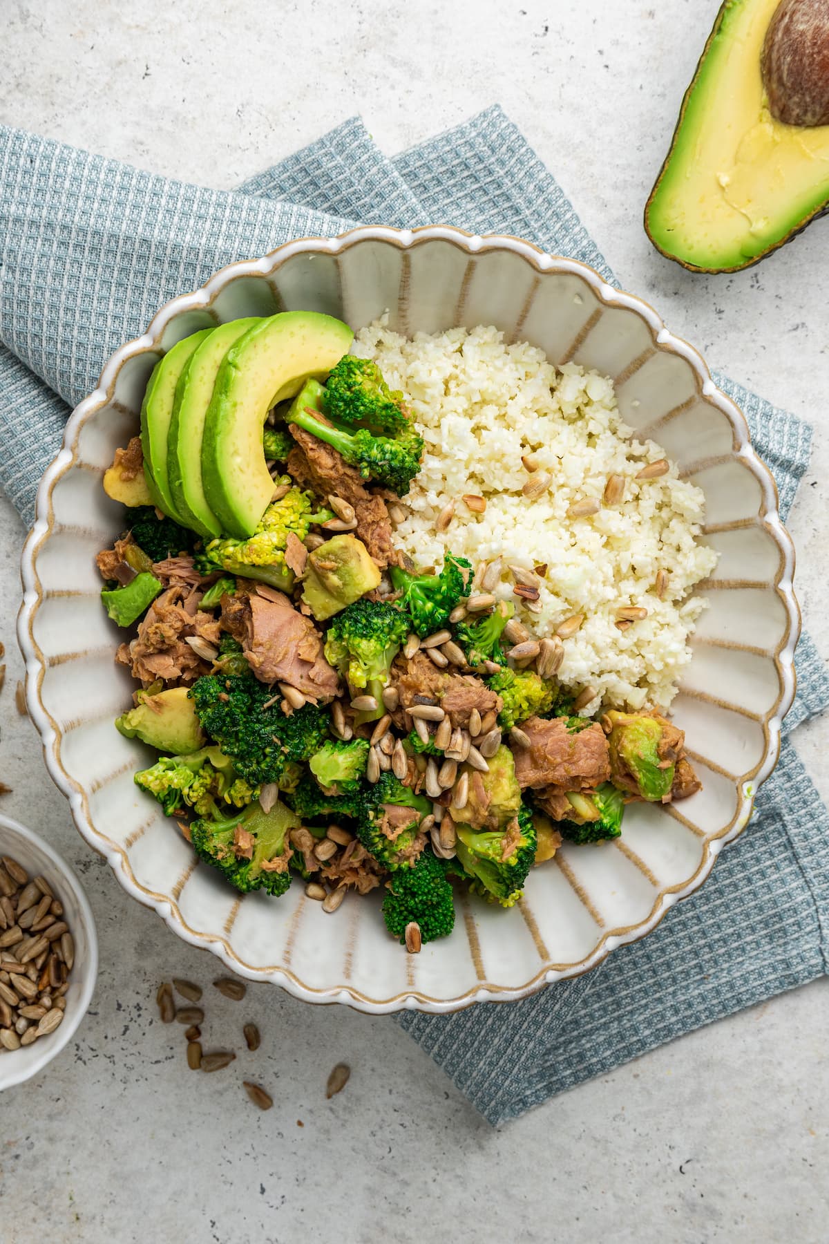 One broccoli avocado tuna bowl topped with sunflower seeds and fresh avocado slices served over rice.