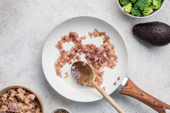 Red onion cooked in a skillet with a wooden spoon.