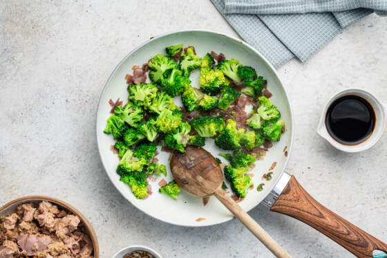 Broccoli and red onion cooked in a skillet with a wooden spoon.