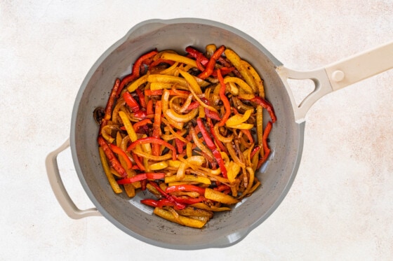 Cooked bell peppers and onions in pan for chicken fajita bowls.