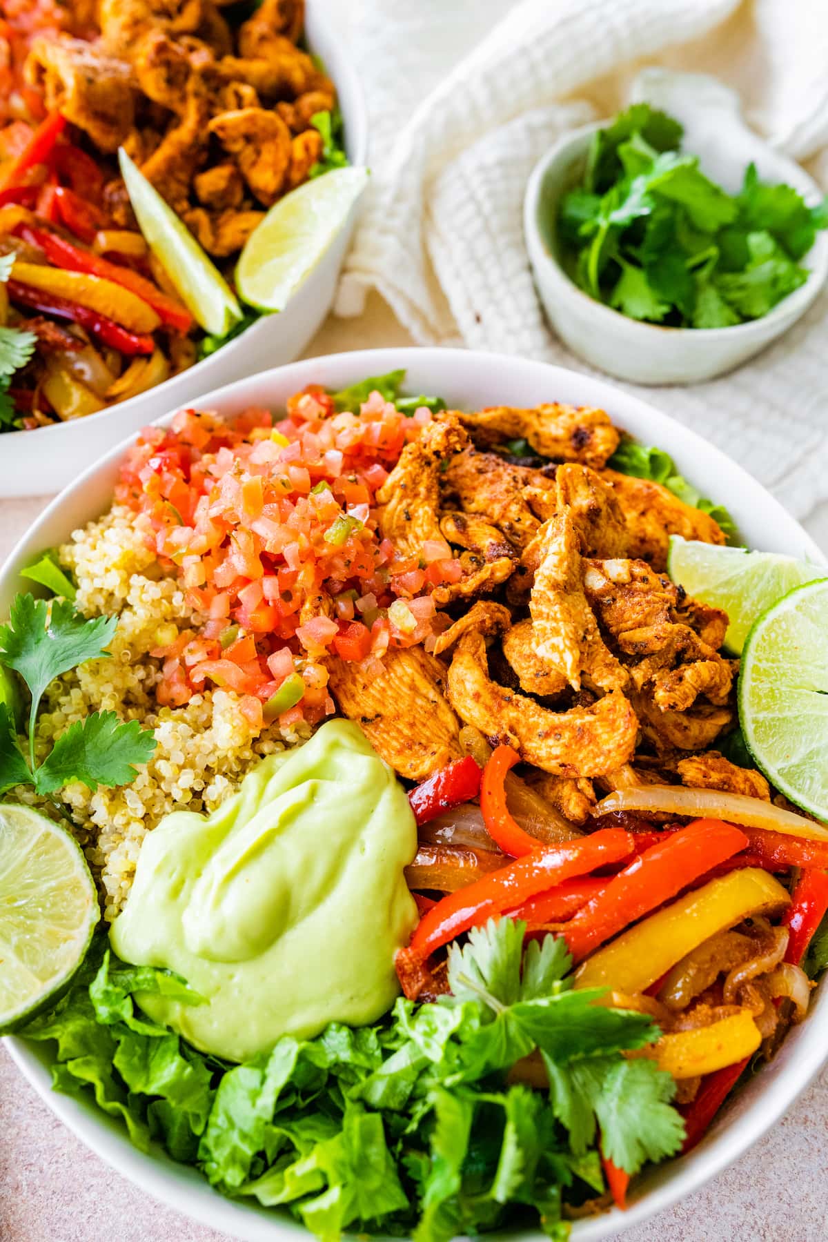 One chicken fajita bowl up close, topped with pico de gallo, avocado sauce, fresh cilantro and lime wedges.