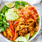 One chicken fajita bowl, topped with pico de gallo, avocado sauce, fresh cilantro and lime wedges.