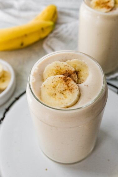 A banana smoothie in a glass, topped with fresh banana slices and a sprinkle of cinnamon.