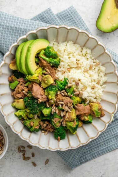 One broccoli avocado tuna bowl topped with sunflower seeds and fresh avocado slices served over rice.