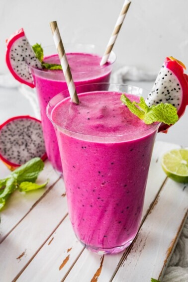 Two dragon fruit smoothies in glasses with straws.
