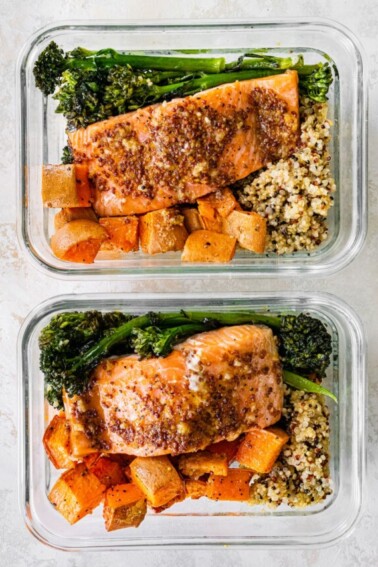 Two glass storage containers with a bed of quinoa topped with roasted sweet potatoes and broccolini and mustard maple salmon.