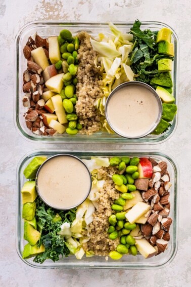 Two glass storage containers layered with detox salad ingredients: almonds, apple, edamame, quinoa, cabbage, kale and avocado. A small container of dressing is also in each of the containers.