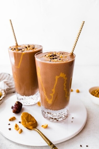 Straight shot of two snickers protein smoothies with drizzle of peanut butter inside glasses.