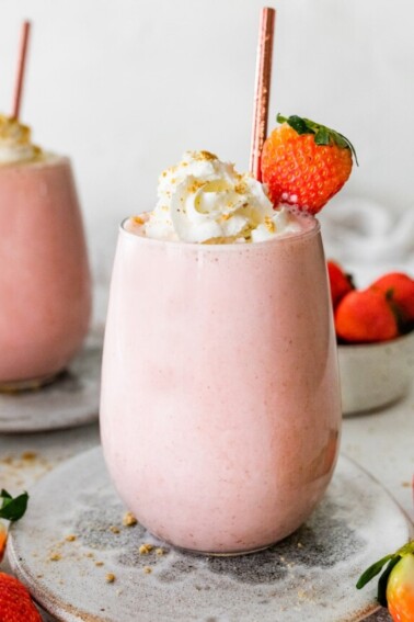 Two strawberry cheesecake smoothies topped with whipped cream and a fresh strawberry.