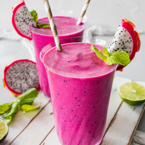 Two dragon fruit smoothies in glasses with straws.