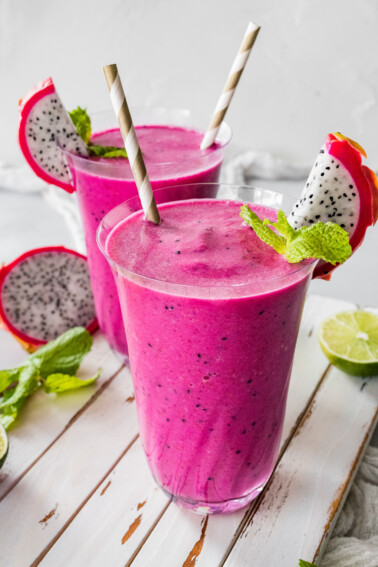 Two dragon fruit smoothies in glasses with straws.