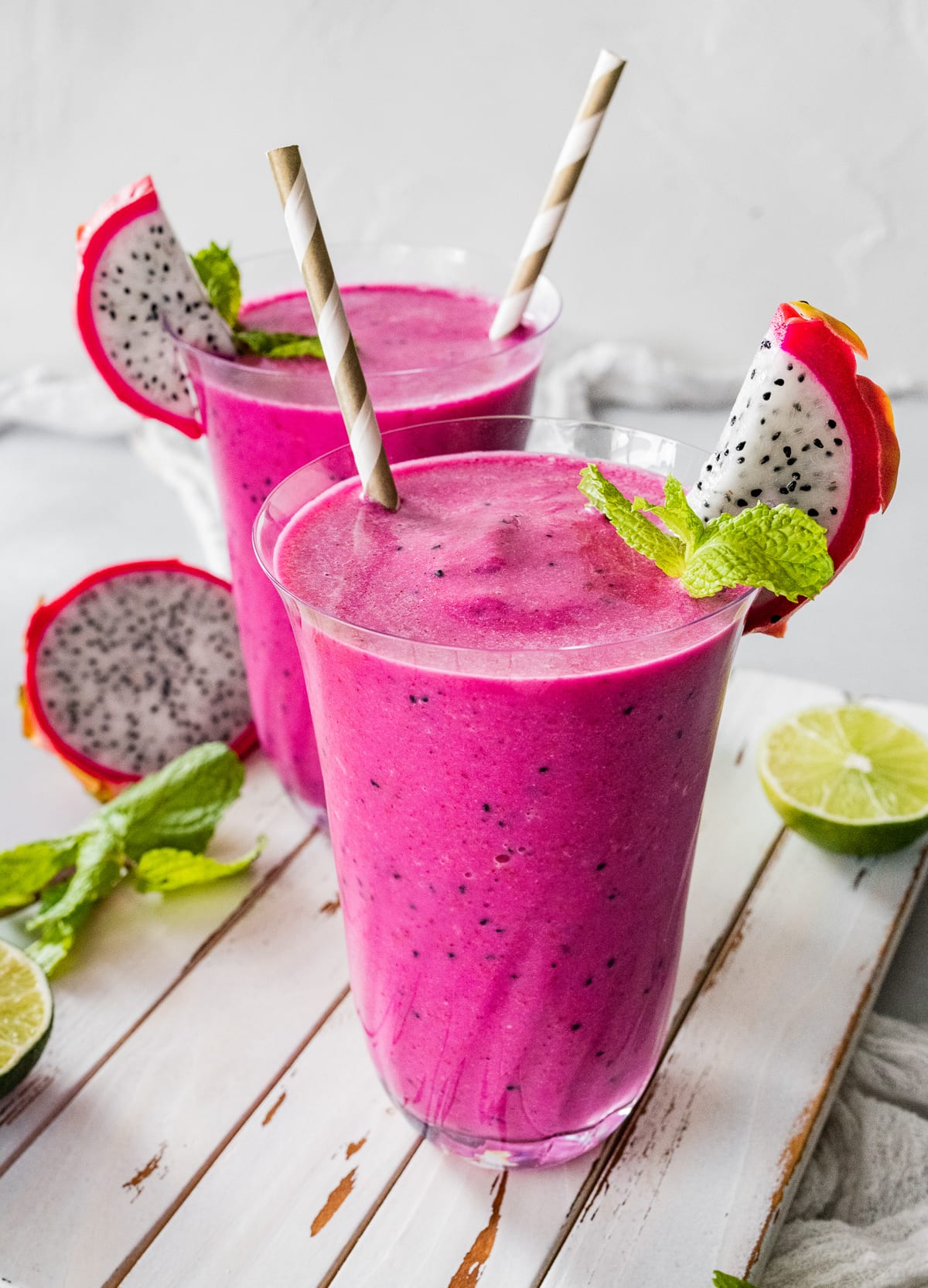 Two dragon fruit smoothies in glasses with straws.