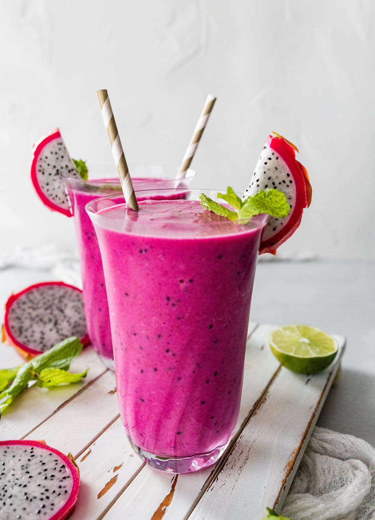 Two dragon fruit smoothies in glasses with straws.