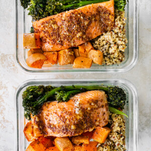 Two glass storage containers with a bed of quinoa topped with roasted sweet potatoes and broccolini and mustard maple salmon.