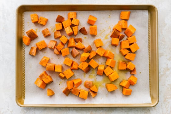 Sweet potato chunks on a parchment-lined baking sheet drizzled with olive oil.