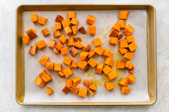 Sweet potato chunks on a parchment-lined baking sheet drizzled with olive oil.