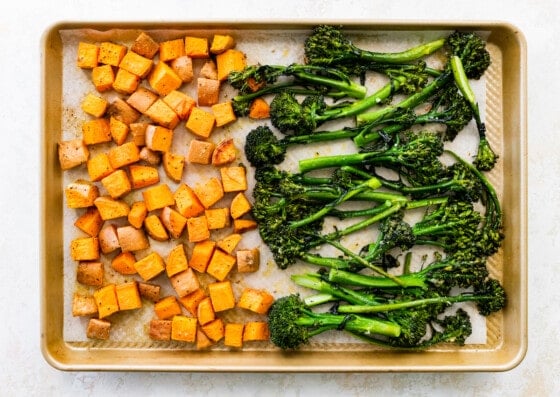 Roasted sweet potatoes and broccolini on a parchment-lined baking sheet.