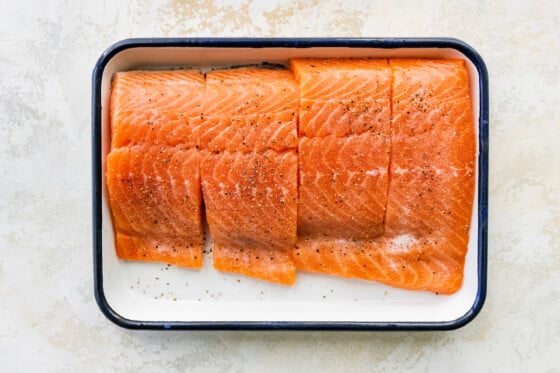 Four chunks of uncooked salmon sprinkled with seasonings in a rectangular baking dish.