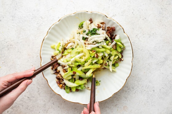 Woman's hands mixing fennel and celery salad in serving bowl.