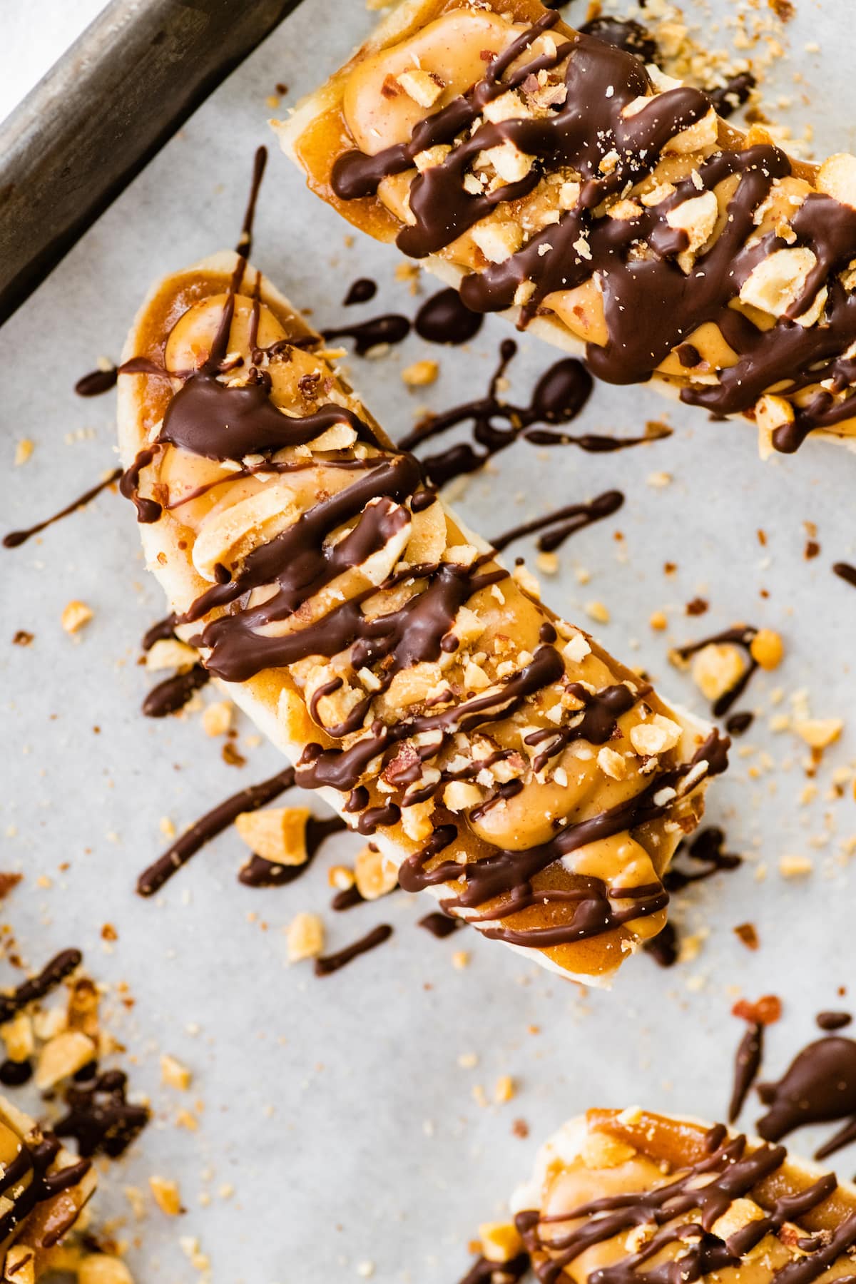 Close up of one frozen banana snickers on a baking tray lined with parchment paper.