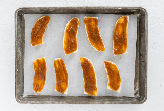 8 banana halves on a baking tray lined with parchment paper each with a layer of date caramel sauce.