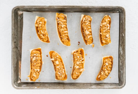 8 banana halves on a baking tray lined with parchment paper each with a layer of date caramel and peanut butter and topped with chopped peanuts.