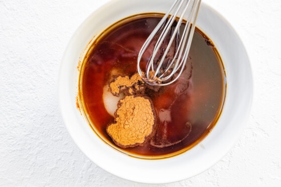 A whisk mixing maple syrup, vanilla, cinnamon, coconut oil and salt in a mixing bowl.