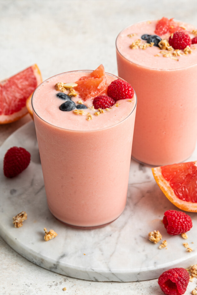 Two grapefruit smoothies topped with fresh berries, grapefruit and granola.