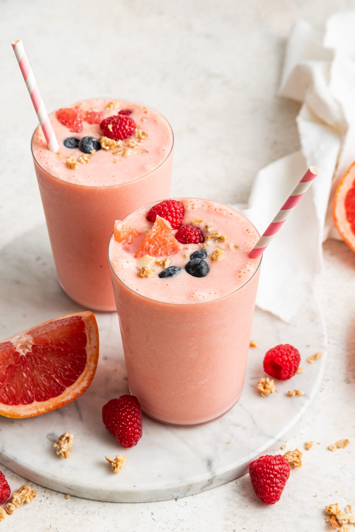 Two grapefruit smoothies with straws served on a marble tray.