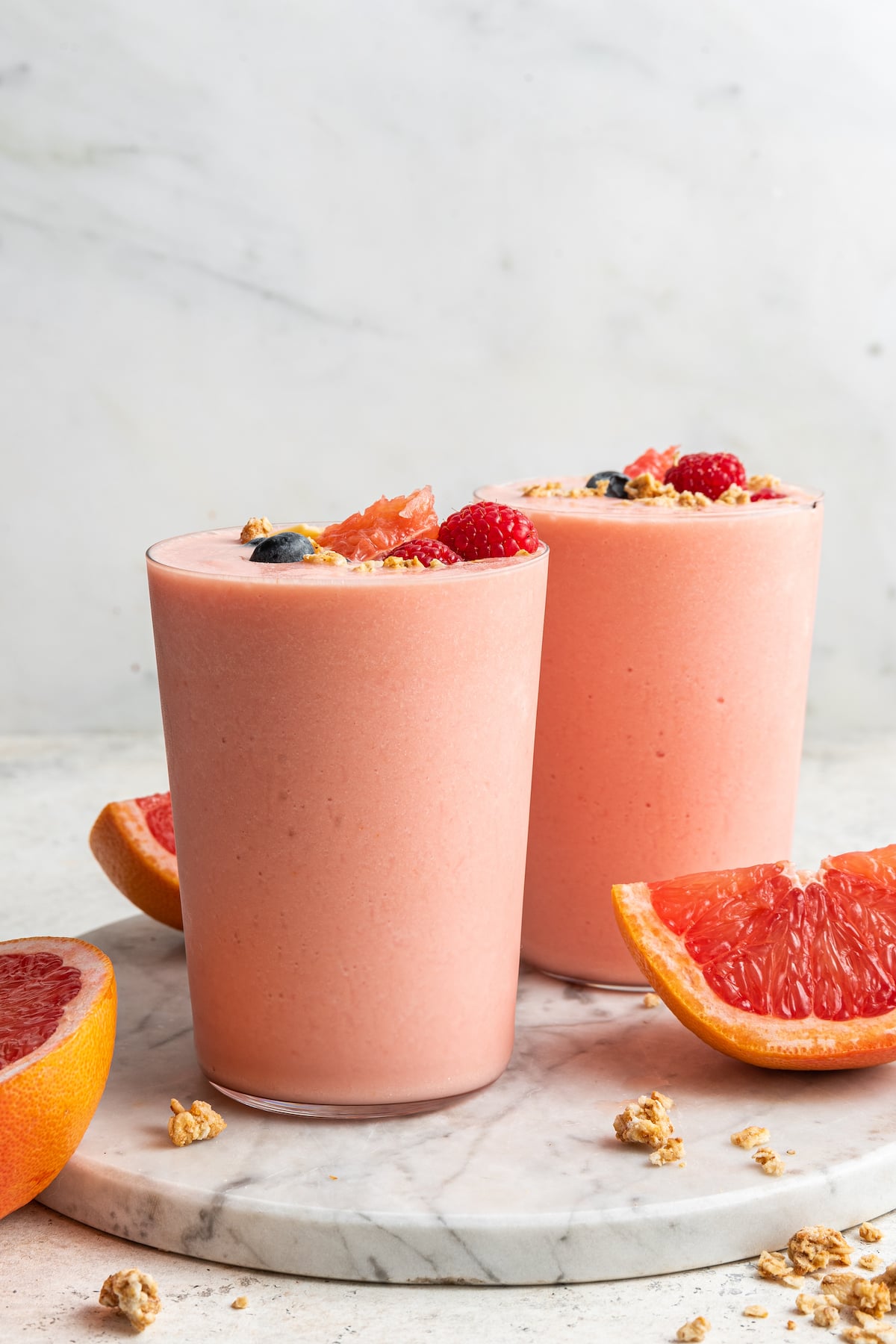 Two grapefruit smoothies with straws served on a marble tray.