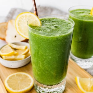 A green lemonade smoothie in a glass with a straw and fresh lemon slice.