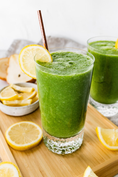 A green lemonade smoothie in a glass with a straw and fresh lemon slice.