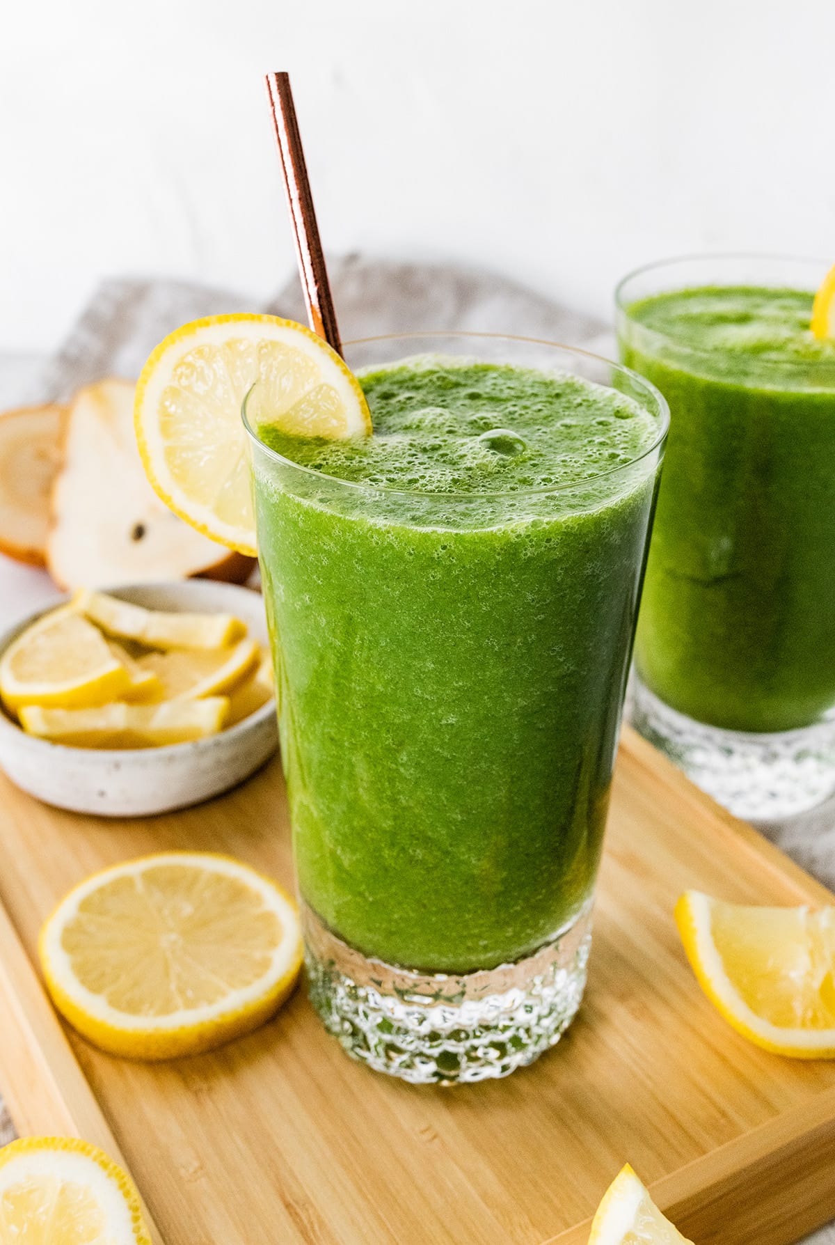 A green lemonade smoothie in a glass with a straw and fresh lemon slice.