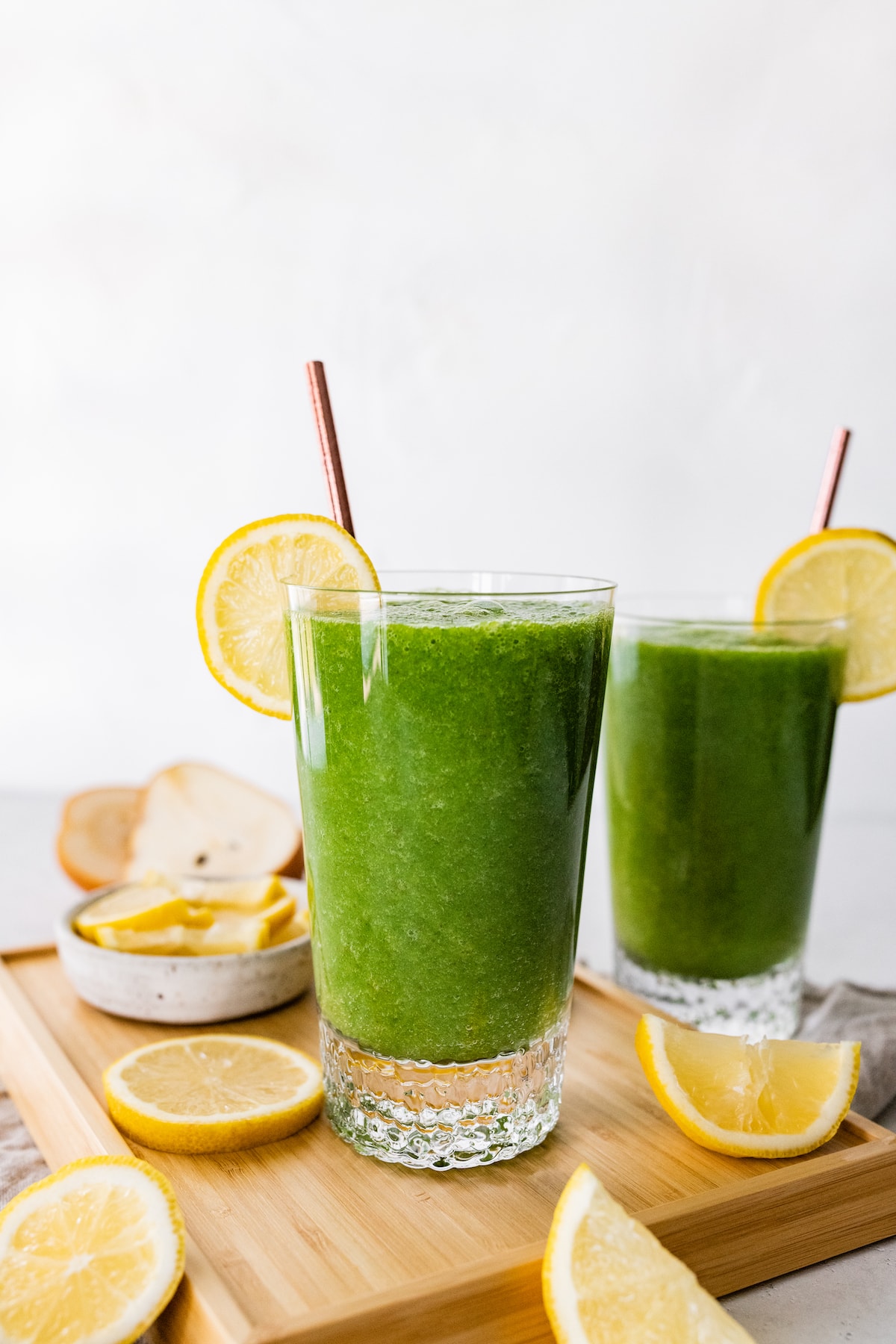 Two green lemonade smoothies in glasses with straws and fresh lemon slices.