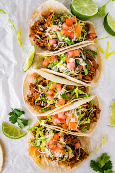 Five ground turkey tacos served in tortillas and topped with lettuce, shredded cheese, tomatoes and cilantro.