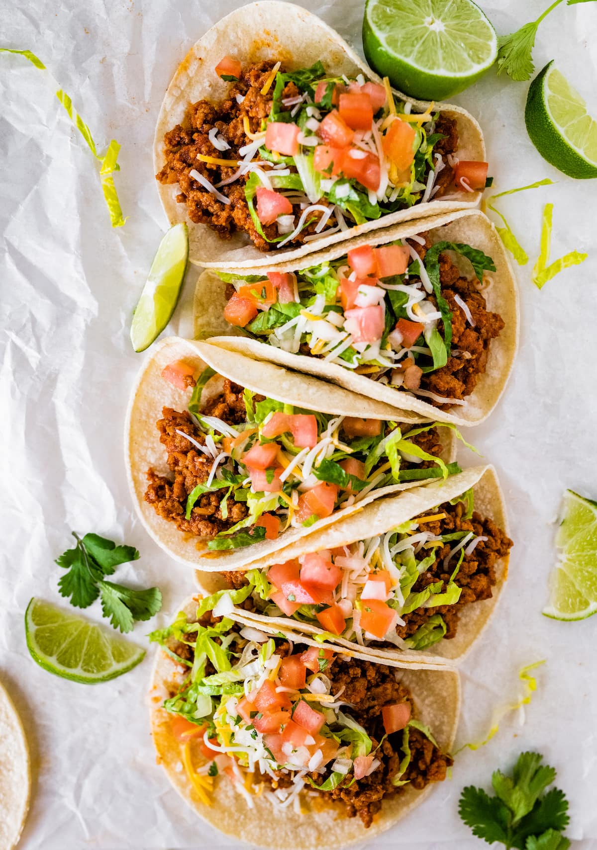 Five ground turkey tacos served in tortillas and topped with lettuce, shredded cheese, tomatoes and cilantro.