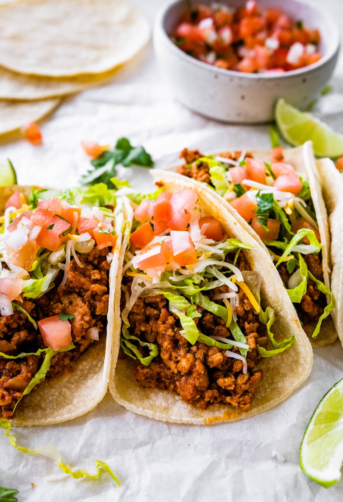 Three ground turkey tacos served in tortillas and topped with lettuce, tomatoes, shredded cheese and cilantro.