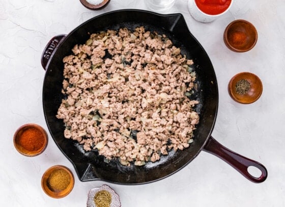 Uncooked ground turkey combined with chopped onions and garlic in a cast iron skillet.