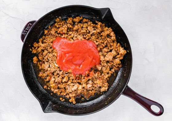 Ground turkey cooking in a cast iron skillet with tomato sauce.