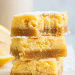 Three lemon bars stacked with a bite taken out of the top bar.