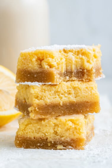 Three lemon bars stacked with a bite taken out of the top bar.