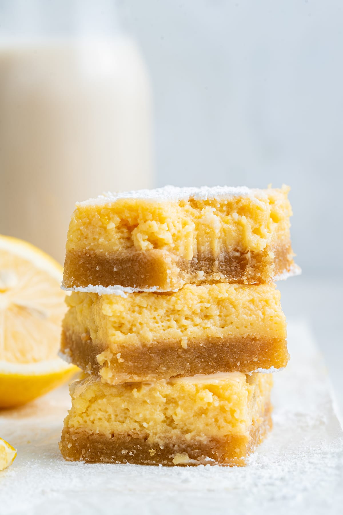 Three lemon bars stacked with a bite taken out of the top bar.