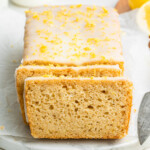 A lemon loaf topped with a lemon glaze and lemon zest. The loaf is cut so you can see the inside of the loaf.