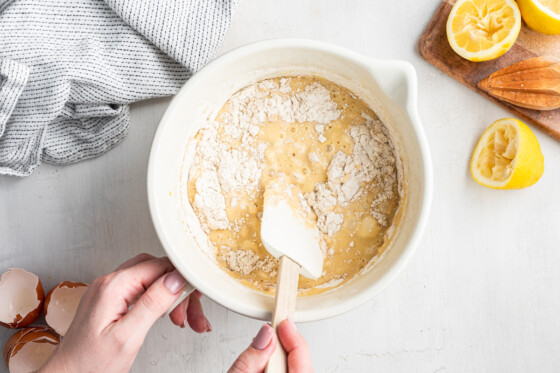 Woman's hand mixing the dry and wet lemon loaf ingredients with a spatula.