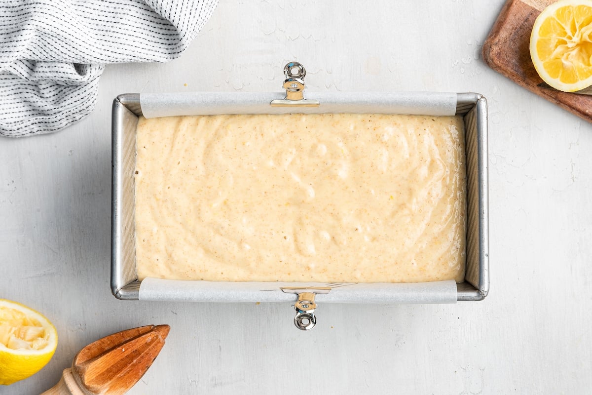 Lemon loaf batter in a loaf pan that's lined with parchment paper waiting to be baked.